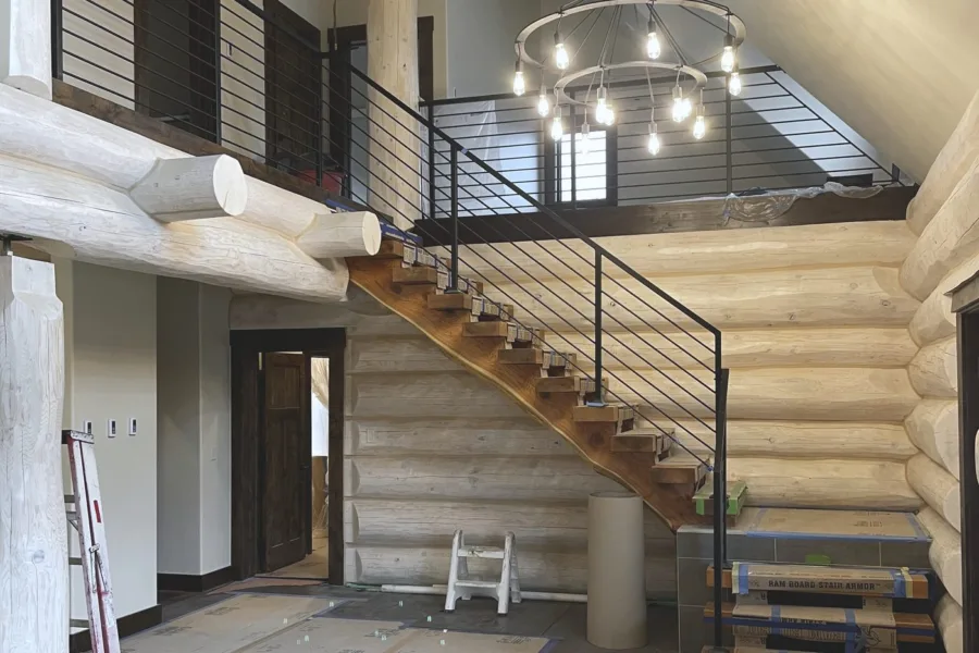 Interior of a log home with an open stair, steel rod rail and a chandelier over the entry