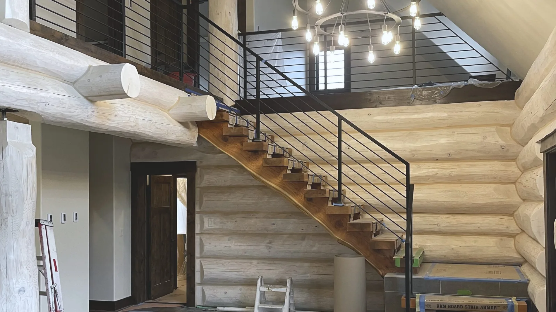 Interior of a log home with an open stair, steel rod rail and a chandelier over the entry
