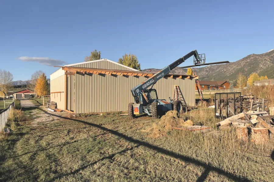 A timber framed covered bay being added to the side of a metal building with a telehandler on site