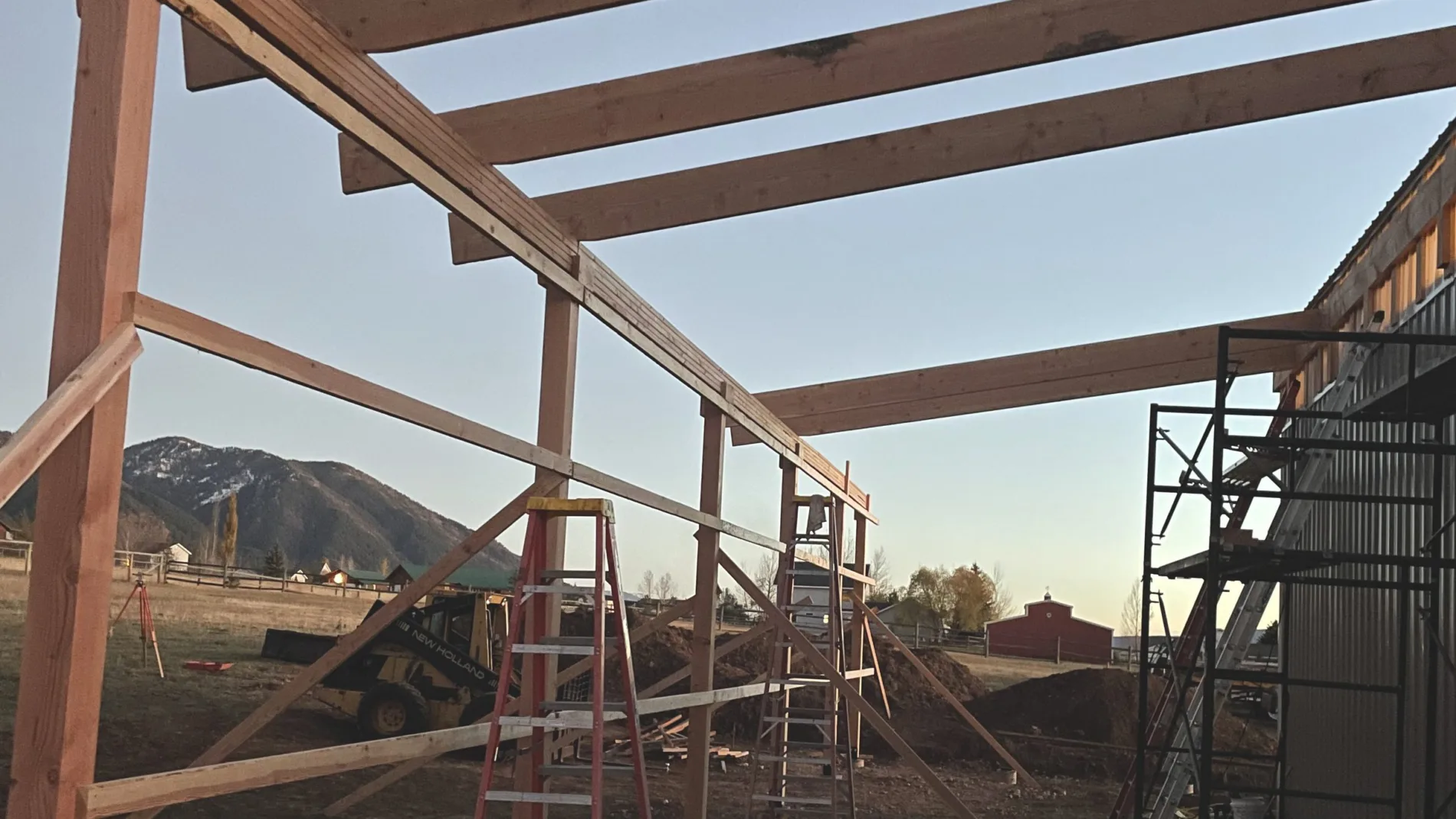 Timber beams framed out from a metal building at dusk with the Star Valley range behind